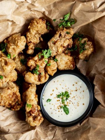 fried gator bites on brown paper garnished with parsley and white sauce