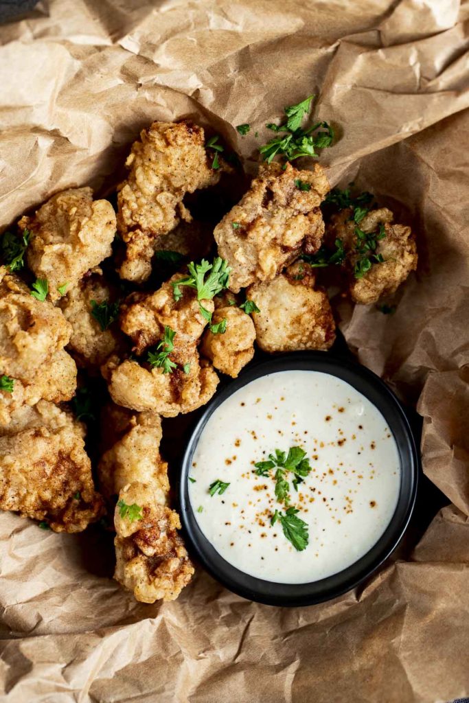 fried gator bites on brown paper garnished with parsley and white sauce
