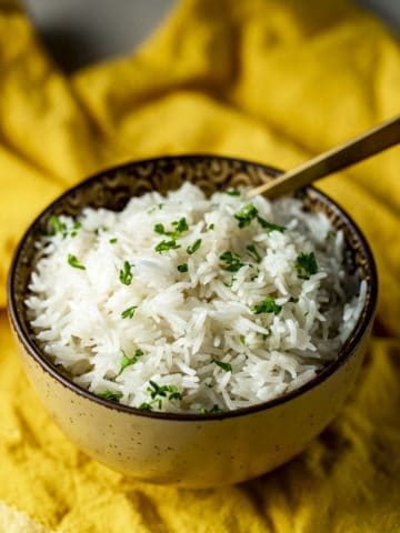A bowl of fluffy basmati rice on a yellow cloth.