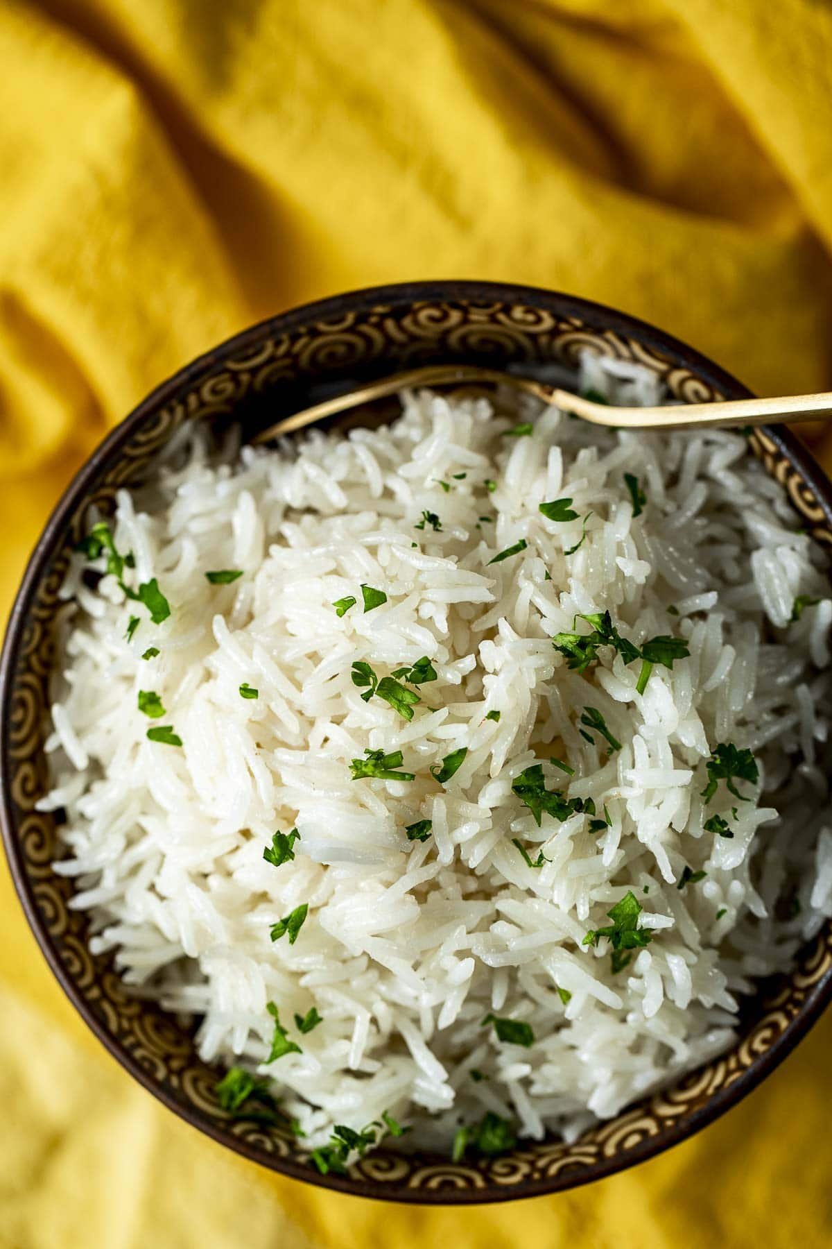Overhead view of basmati rice in a bowl and topped with chopped fresh herbs.