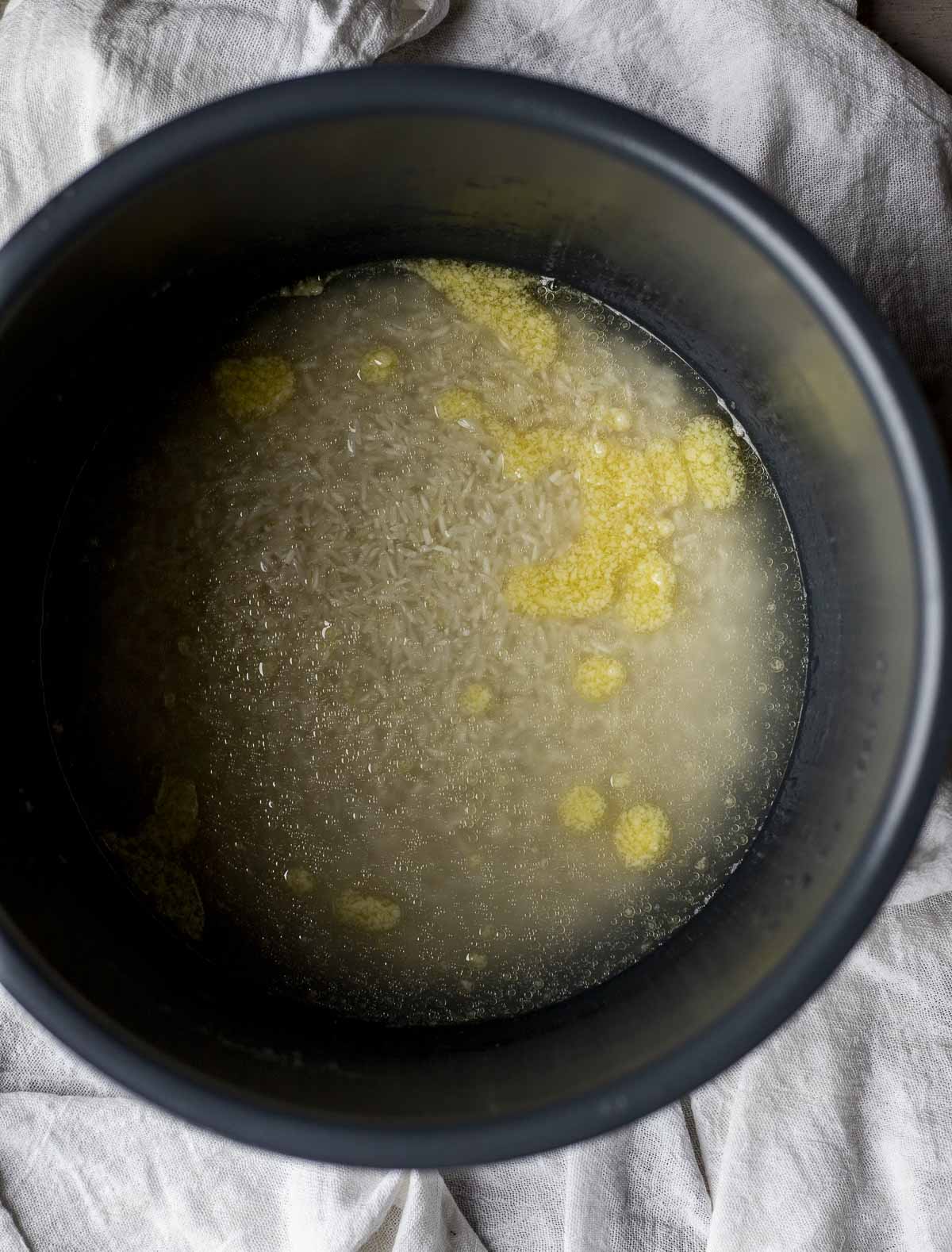 Uncooked basmati rice, ghee, salt and water in an Instant Pot insert.