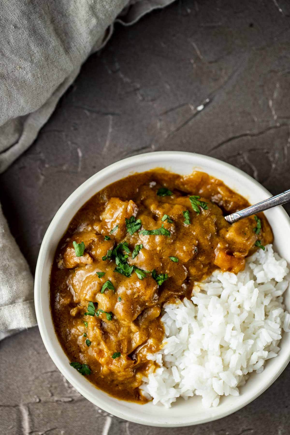 chicken and vegetables in orange curry sauce with rice in a bowl with a spoon