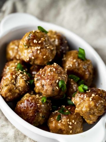 a bowl of glazed meatballs and green onions