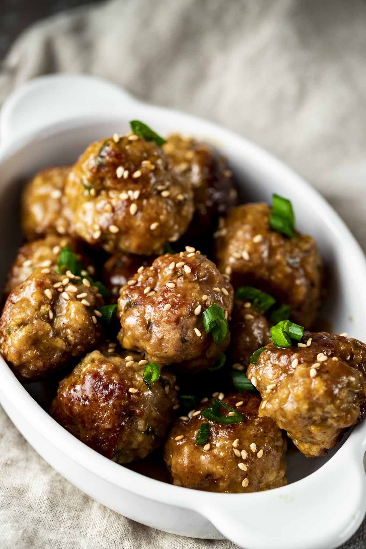 a bowl of glazed meatballs and green onions