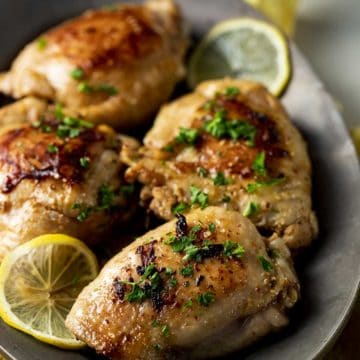 Sous vide chicken thighs served with chopped herbs and lemon slices.