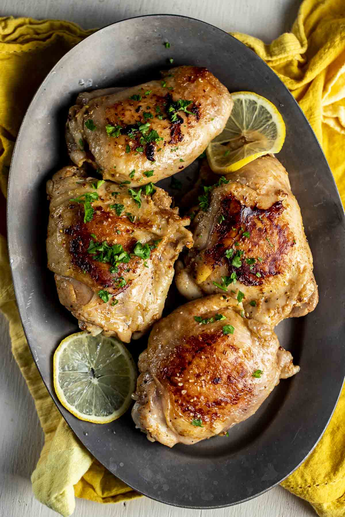 Four browned chicken thighs arranged on a platter with lemon slices.