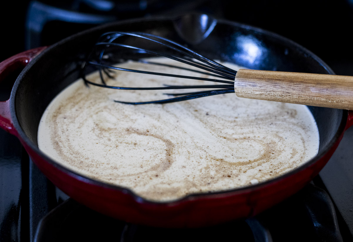 a skillet with a white cream sauce in it and a whisk
