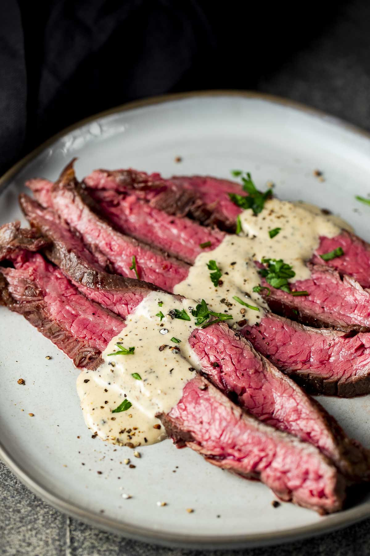 slices of medium rare beef on a plate with cream sauce and parsley