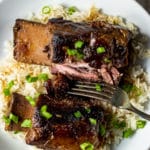 Two sous vide short ribs on a plate with rice and a fork.