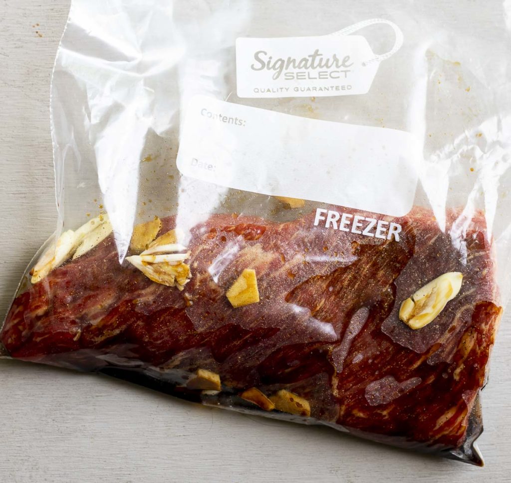 raw beef in a clear plastic bag with garlic pieces