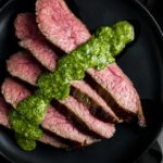 slices of rare beef on a plate with chimichurri sauce