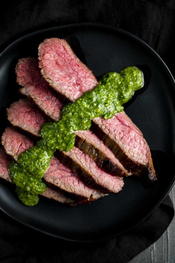 slices of rare beef on a plate with chimichurri sauce