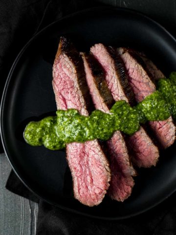 a plate of sliced rare beef drizzled in green sauce
