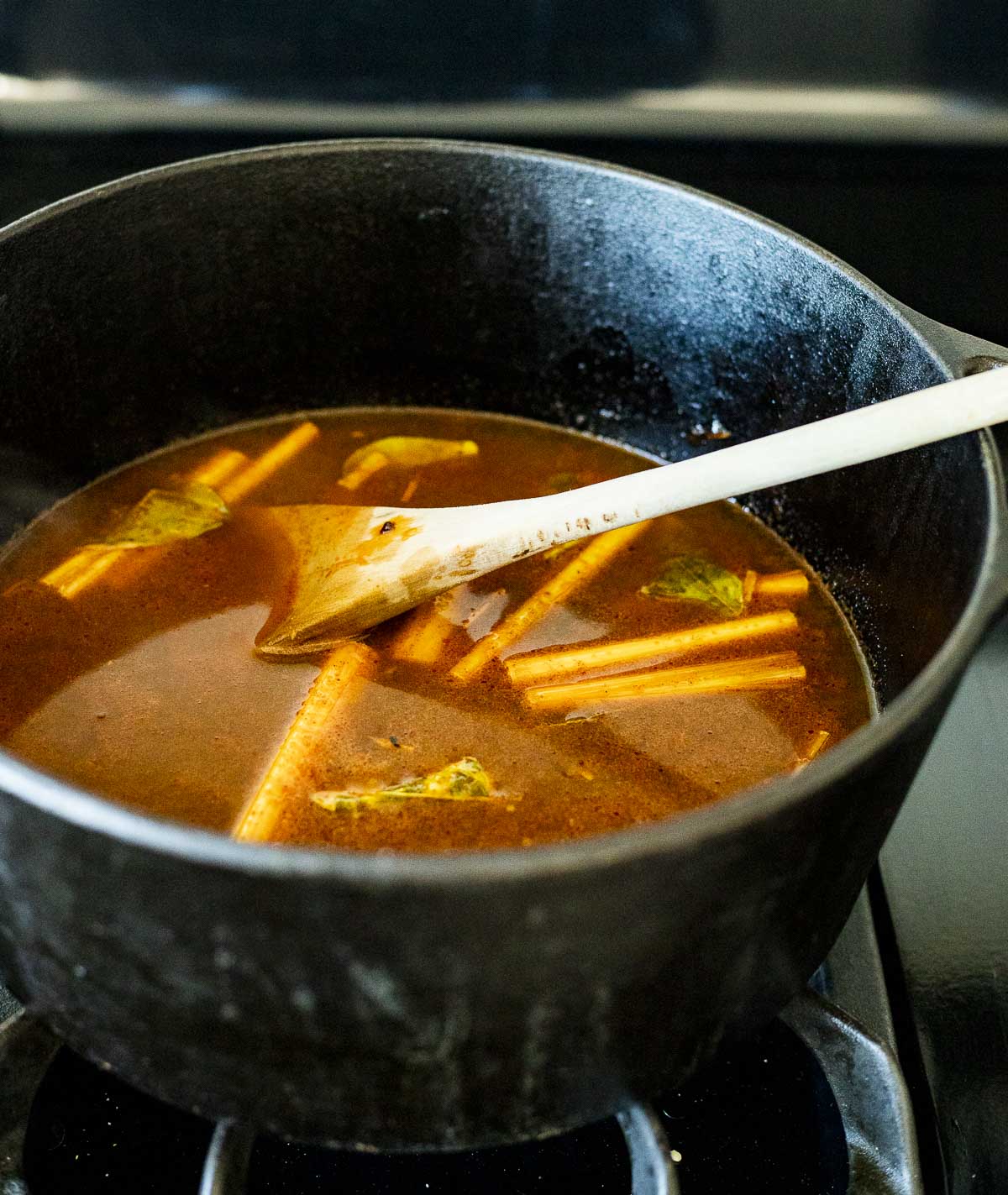 Tom yum soup broth in a pot on the stovetop with a wooden spoon inserted into it.