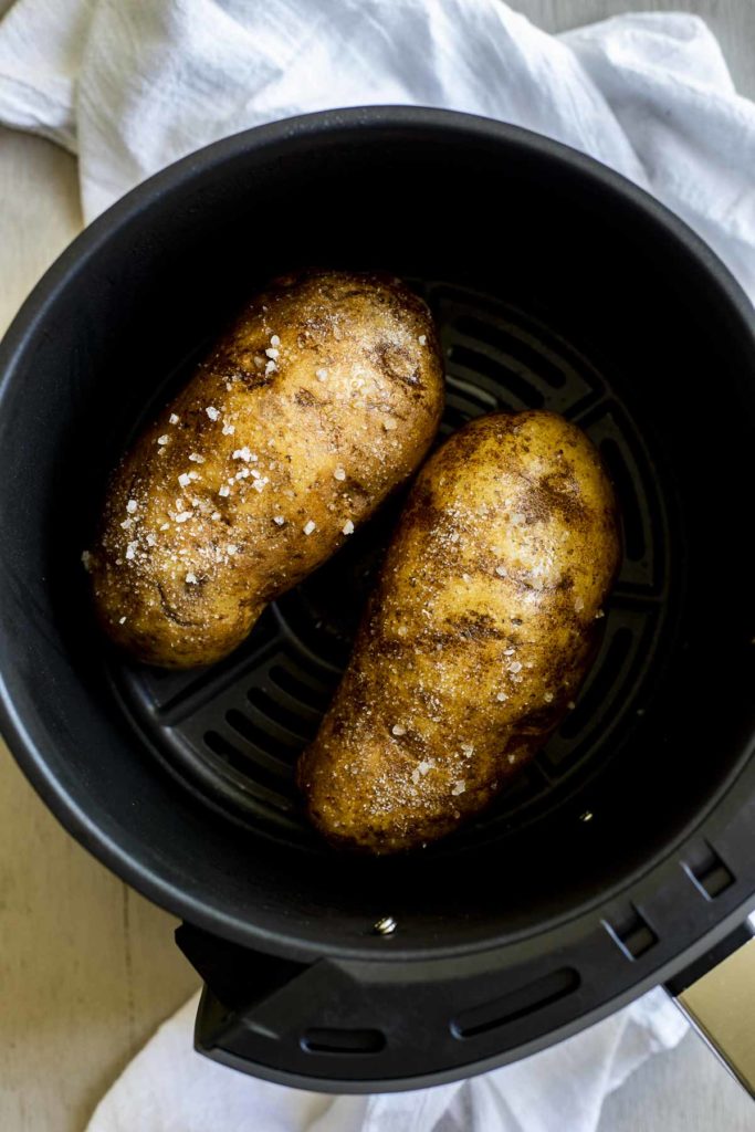 2 potatoes in an air fryer basket with salt on them