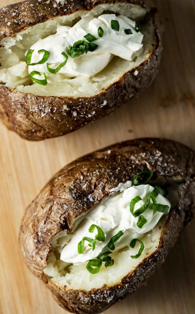 2 baked potatoes with sour cream on a wood board