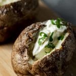 2 air fryer baked potatoes on a board filled with sour cream and green onions