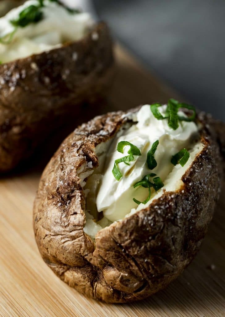 2 air fryer baked potatoes on a board filled with sour cream and green onions