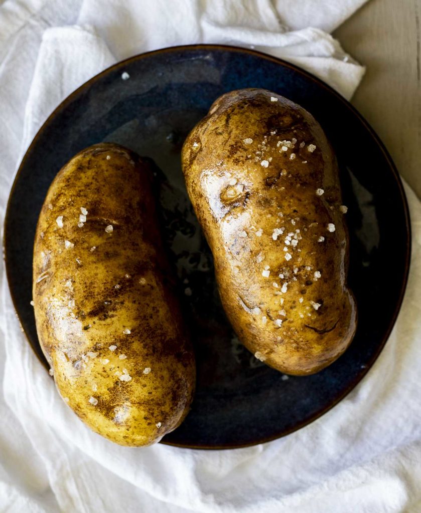 2 potatoes on a plate covered in oil and salt