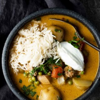 a bowl of orange colored soup with yogurt, rice and potatoes garnished with cilantro