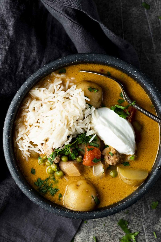 a bowl of orange colored soup with yogurt, rice and potatoes garnished with cilantro