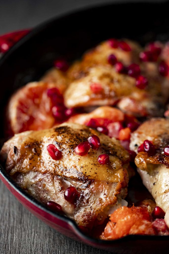 browned chicken thighs in a skillet garnished with pomegranate seeds