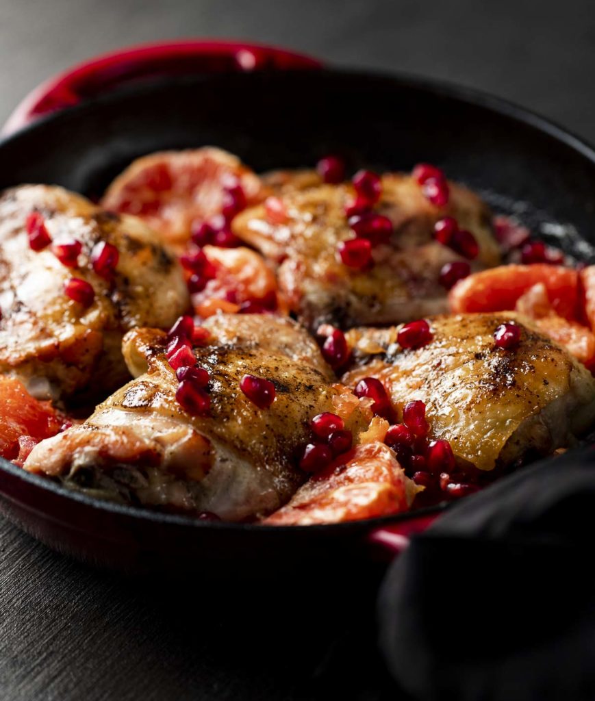 4 chicken thighs in a skillet with pomegranate seeds and grapefruit