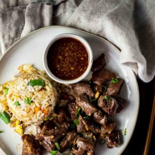a plate of beef pieces with fried rice and brown sauce on the side