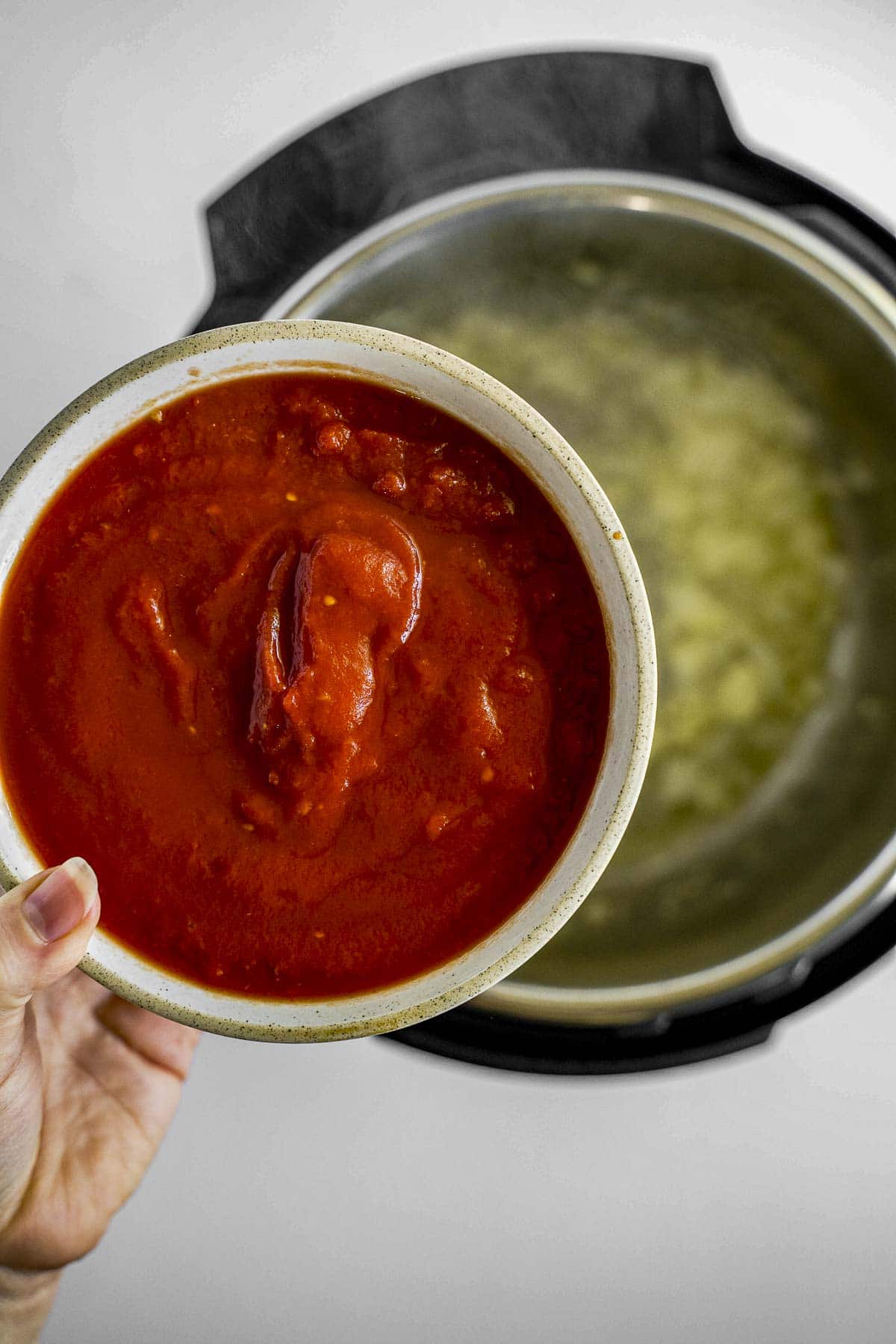 Adding in tomato puree to the pressure cooker.