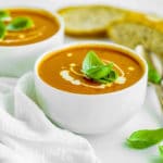 Two bowls of tomato soup with cream and basil as garnish.