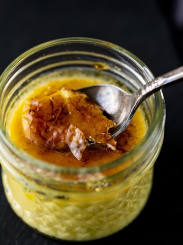 a spoon cracking the top of a glass jar of creme brulee