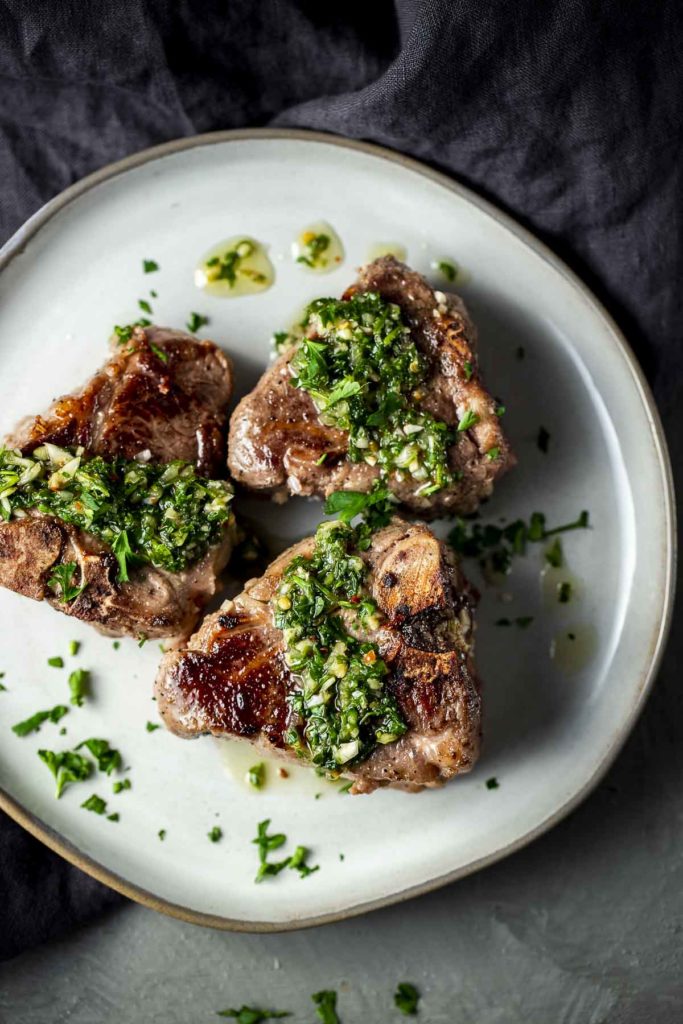 green chimichurri sauce drizzled over lamb chops on a plate