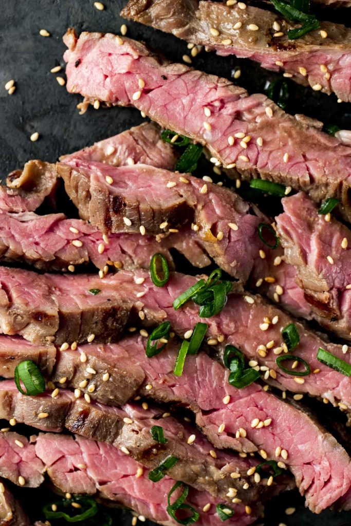Close up of sliced skirt steak with chopped green onion on top.