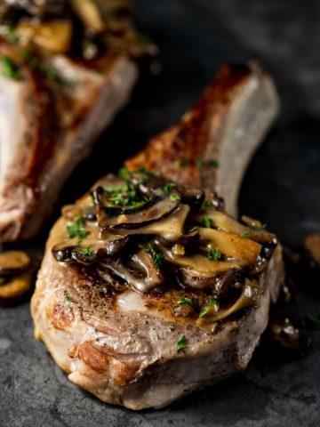 veal chop on a board with mushrooms and parsley on top