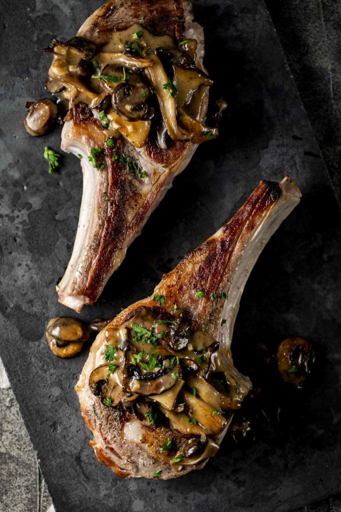 2 veal chops on a baord garnished with parsley and mushrooms