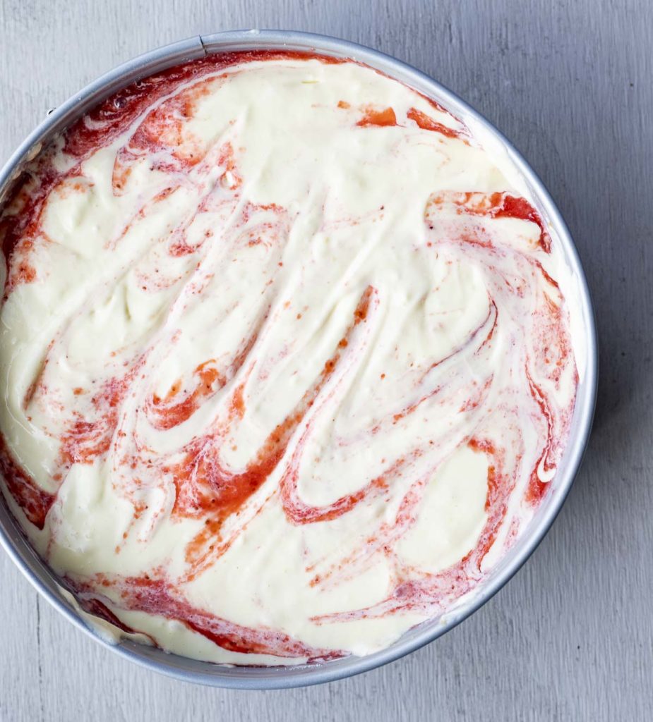 white and red swirled cheesecake filling in a springform pan