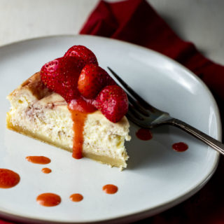 a piece of cheesecake on a plate drizzled with fresh strawberries