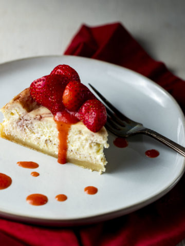 a piece of cheesecake on a plate drizzled with fresh strawberries