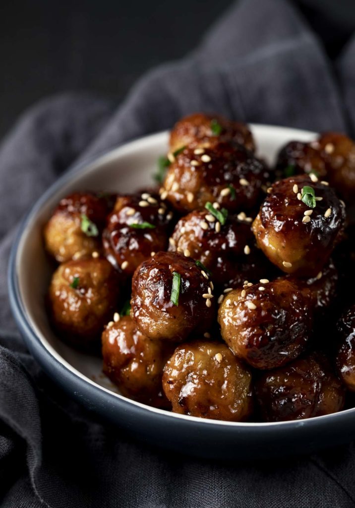 a bowl of meatballs with glaze on them and sesame seeds