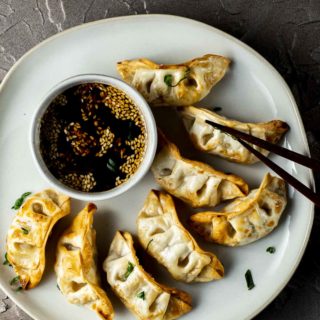 a plate of cooked potstickers with chopsticks and brown dipping sauce