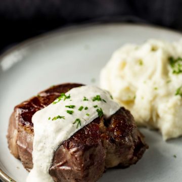 filet mignon on a plate with mashed potatoes and white sauce