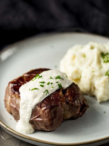 filet mignon on a plate with mashed potatoes and white sauce