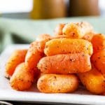 Side view of glazed baby carrots on a white plate.