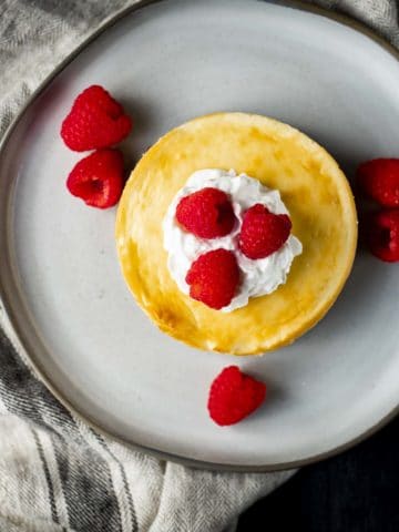Overhead view of a cheesecake made in an air fryer with whipped cream and raspberries on top.