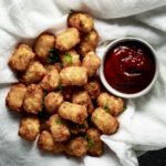 Air fryer tater tots beside a serving of ketchup.