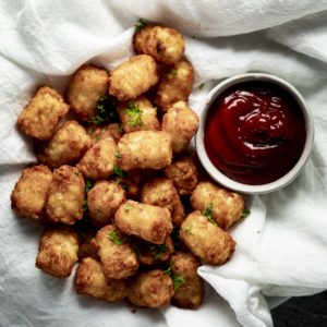 Air fryer tater tots beside a serving of ketchup.