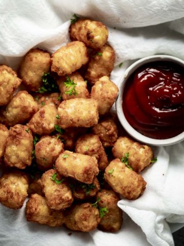 Air fryer tater tots beside a serving of ketchup.