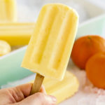 Hand holding up an orange creamsicle popsicles.