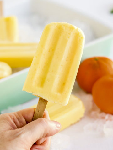 Hand holding up an orange creamsicle popsicles.