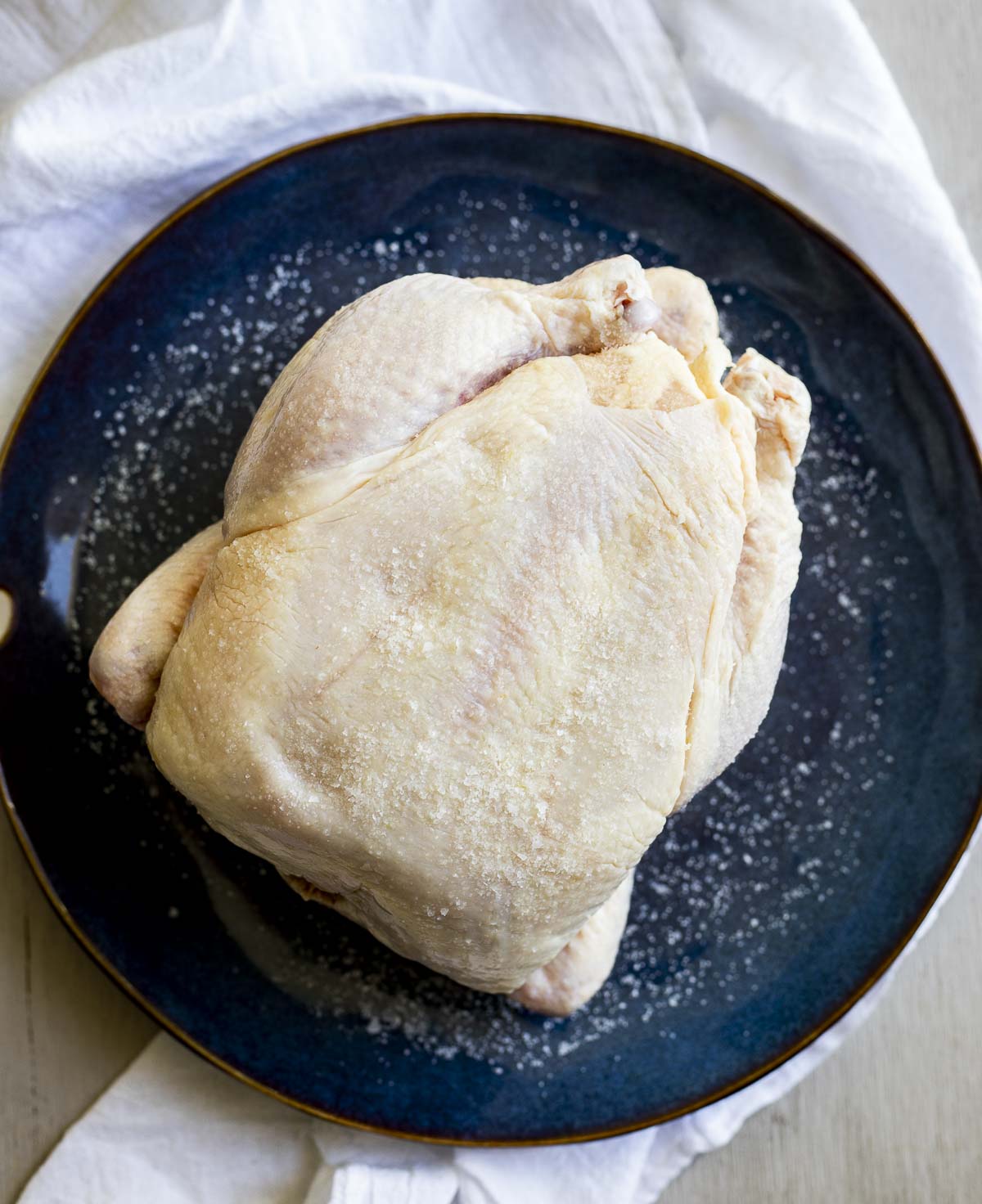 Raw whole chicken on a plate rubbed with salt.